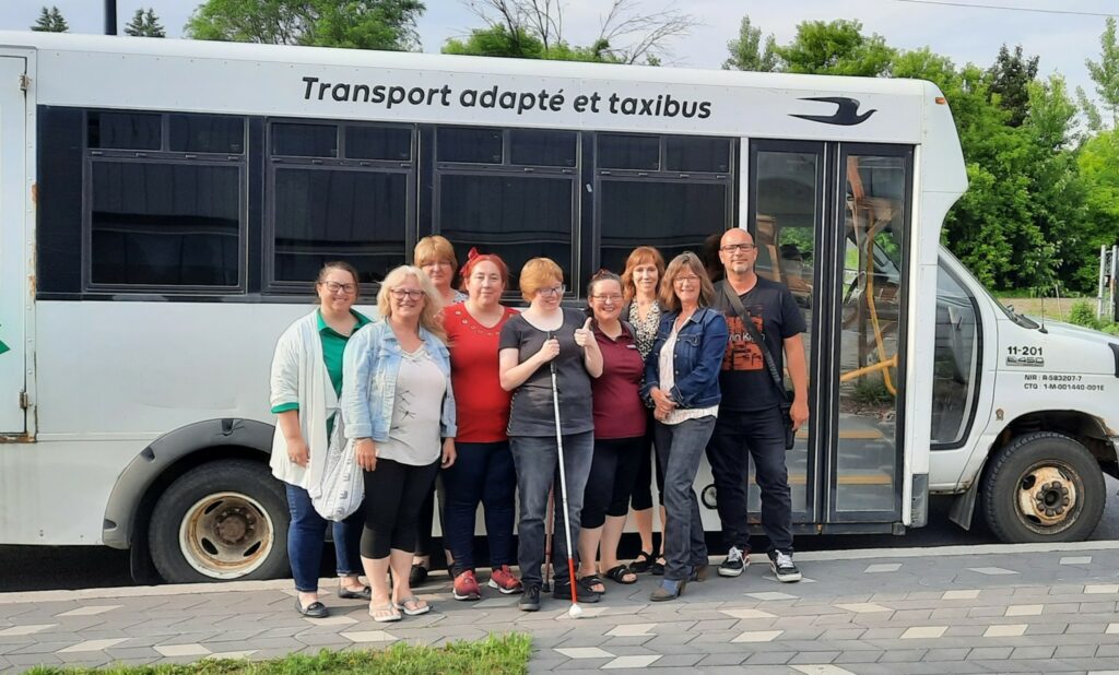 Groupe de personnes devant un bus se nommant: transport adapté et taxibus